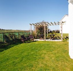A garden area with grass lawn a wooden pergola two wooden chairs and two small tables at Eleri in Abersoch