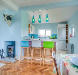 Kitchen and dining area with wooden floor and colorful chairs at Gilfach in Abersoch