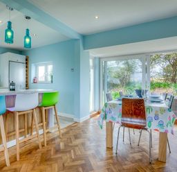 A kitchen and dining area with bar stools and a large window overlooking a garden at Gilfach in Abersoch
