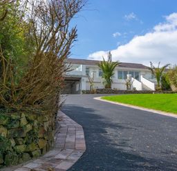 A driveway leading to a white house with palm trees and a green lawn at 3 Madoc View Bwlchtocyn near Abersoch