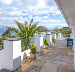 A patio with stone tile flooring and potted plants overlooking trees and the ocean at 3 Madoc View in Bwlchtocyn near Abersoch