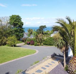 A garden with a palm tree lawn and driveway overlooking the sea at 3 Madoc View in Bwlchtocyn near Abersoch