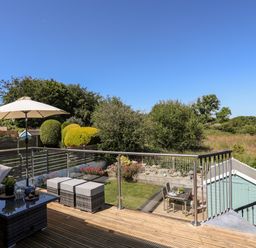 An outdoor deck with seating and an umbrella overlooking a garden and green landscape at The Anchorage in Abersoch