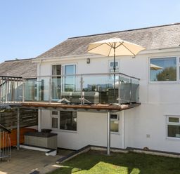 A balcony with glass railing and umbrella with spiral staircase leading to a patio below at The Anchorage in Abersoch