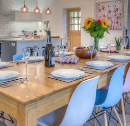 A dining table set with plates cutlery and glasses with colorful chairs in a kitchen at The Coach House in Abersoch