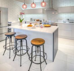 A modern kitchen with a central island with three stools a refrigerator oven and white tiled walls at The Coach House in Abersoch