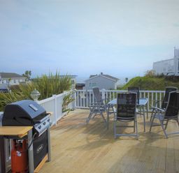 An outdoor patio with a gas grill and a table with six chairs on a wooden deck at The Warren D26 in Abersoch