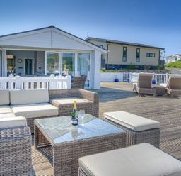 An outdoor patio with wicker seating, a glass table, and a bottle with glasses at The Warren Q4 in Abersoch
