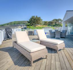 An outdoor deck with two lounge chairs a dining table with chairs and a barbecue grill at The Warren Q4 in Abersoch