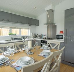 A kitchen with a dining table set with glassware and plates next to grey cabinets and appliances at The Warren T23 in Abersoch