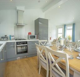 A kitchen and dining area with grey cabinets a dining table set for six and a living area with windows at The Warren T23 in Abersoch