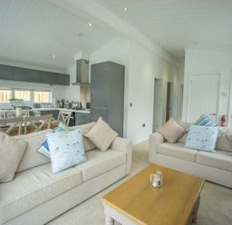 A living room with two beige sofas and a wooden coffee table in an open plan kitchen and dining area at The Warren T23 in Abersoch