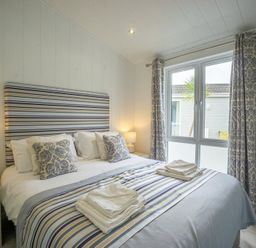 A bedroom with a double bed striped headboard bedside tables lamps and patterned curtains at The Warren T23 in Abersoch