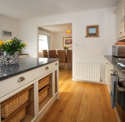A kitchen with wooden floor granite countertops dining area with wicker chairs in the background at Ty Coed in Abersoch