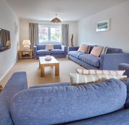 A living room with blue sofas and wooden table near a window at Ty Coed in Abersoch