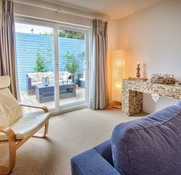 A living room with a cream armchair blue sofa stone mantel and sliding glass doors to outdoor seating at Ty Coed in Abersoch