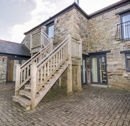 An outdoor courtyard with stone walls wooden staircase and multiple windows at Beacon Barn in St Agnes