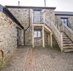 An outdoor stone courtyard with wooden stairs leading to an upper door at Beacon Barn in St Agnes