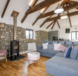 A living room with a grey sofa pink armchair wood burning stove and exposed stone walls at Beacon Barn in St Agnes