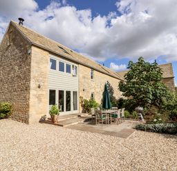 Stone house with a patio set and umbrella outside and gravel driveway at Stow Cottage Barn in Churchill Oxfordshire