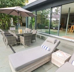An outdoor patio with lounge chairs and dining table under umbrella next to glass sliding doors at Landmark Salcombe