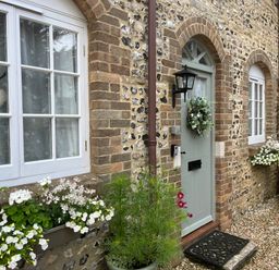 A stone and brick house facade with white windows flower boxes and a green door with a wreath at The Coach House at Lackington Farm Piddletrenthide