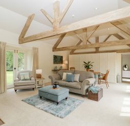 A living room with a sofa armchair ottoman rug dining table chairs and exposed wooden beams at The Shippon in Honiton