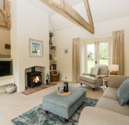 A living room with sofa armchair ottoman fireplace and television at The Shippon in Honiton
