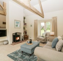 A living room with a wood burning stove a television a grey armchair a beige sofa and a blue ottoman at The Shippon in Honiton