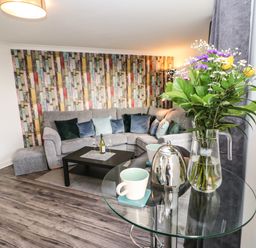A living room with a grey sofa and colorful wallpaper at Sandy Corner in Blyth Northumberland