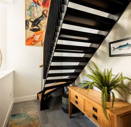 A hallway with a black metal staircase a wooden sideboard with a green plant and artwork on the walls at Church Rooms in Port Isaac