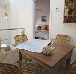 A dining area with a wooden table and four wicker chairs a map and bowl on the table a bedroom visible through doorway at The Barn 20 At The Beach Torcross