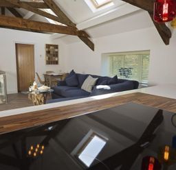 A kitchen with a wooden countertop and hob overlooking a living area with a blue couch and wooden beams at The Barn 20 At The Beach Torcross
