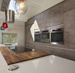 A kitchen with built in ovens wooden countertop and colorful pendant lights at The Barn 20 At The Beach Torcross
