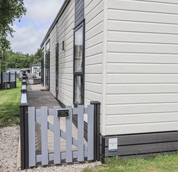 A gate and deck outside a lodge with grass and other lodges at Yealands 27 South Lakeland Leisure Village near Carnforth