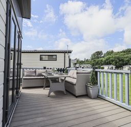 An outdoor deck with a glass table and two sofas surrounded by a fence at Yealands 27 South Lakeland Leisure Village near Carnforth