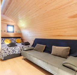 A bedroom with a bed and sofa against wooden walls at Sea View in St Buryan