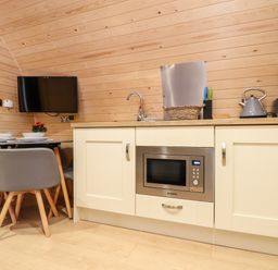 A kitchenette with a microwave oven, sink, kettle, table with chairs and a wall-mounted TV at Sea View in St Buryan