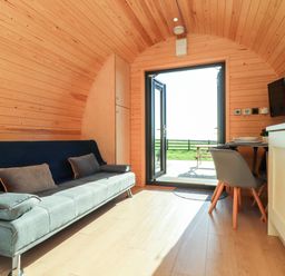 A small wooden room with a gray sofa and pillows a dining table with chairs a TV mounted on the wall and open doors leading outside at Sea View in St Buryan