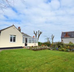 A single story house with a garden and flower beds under a cloudy sky at Hafod Cottage in Cemaes Bay