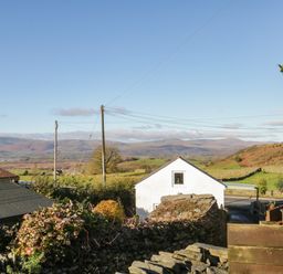 A view of hills and fields with a white building and stone walls under a clear sky at Brookside in Grizebeck