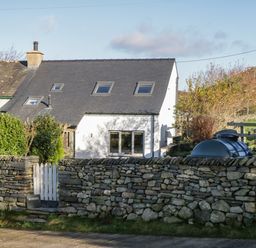 A white house with a slate roof behind a stone wall and a white picket gate at Brookside in Grizebeck