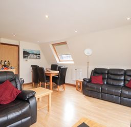 A living room with black leather sofas and red cushions a wooden dining table with black chairs and a wooden floor at Owl Lodge in South Laggan near Invergarry