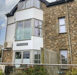 A building with stone and white walls with windows and a sign that says Four Seasons at 7 Four Seasons in Carbis Bay