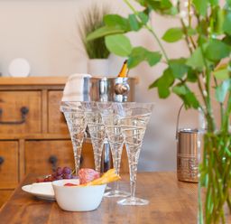 A wooden table with four champagne glasses grapes snacks and a vase with green leaves at 7 Four Seasons in Carbis Bay