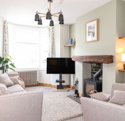 A living room with two sofas a TV a wood burning stove and a large window at Dovestones in Keswick