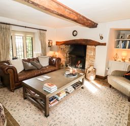 A living room with a brown leather sofa gray armchair coffee table and fireplace at The Small House Near Bourton-On-The-Water