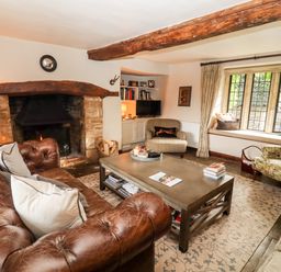 A living room with a leather sofa a stone fireplace wooden beams and a window seat at The Small House Near Bourton-On-The-Water