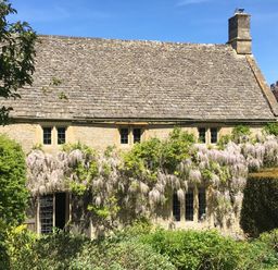 A stone house with climbing plants and flowers on the front surrounded by greenery at The Small House Near Bourton-On-The-Water