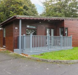 A wooden cabin with a small porch and railing surrounded by grass and trees at Bugle in Saltburn-By-The-Sea
